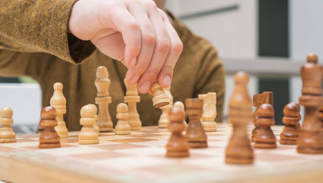 Hand of child move white pawn on wooden chessboard.