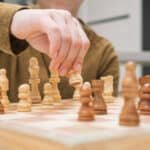 Hand of child move white pawn on wooden chessboard.