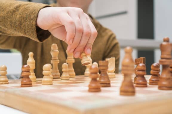 Hand of child move white pawn on wooden chessboard.